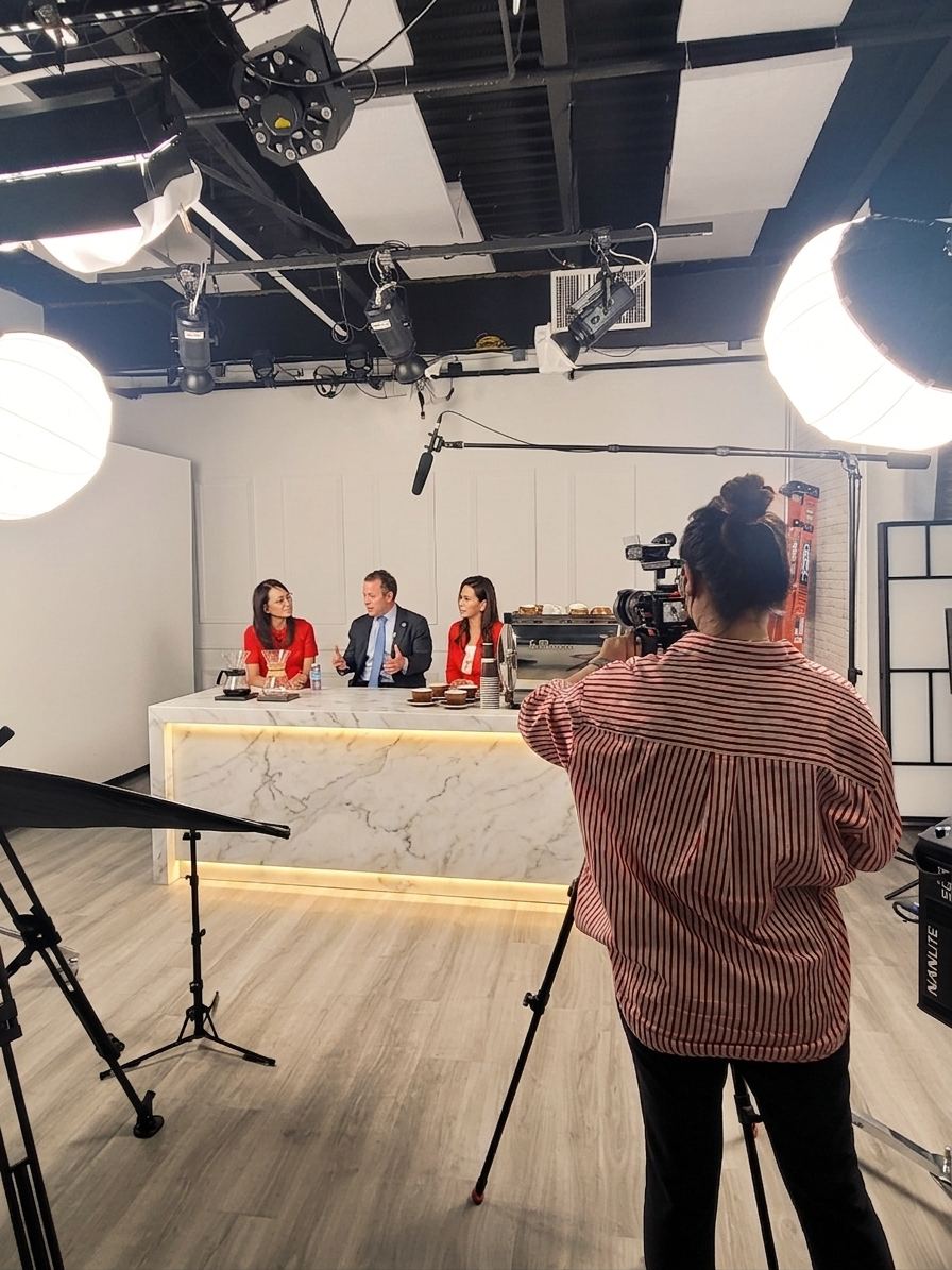 Three hosts at the anchor desk being filmed by a camera operator